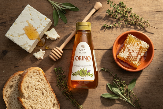 Orino Greek Mountain Honey jar surrounded by PDO feta with honey drizzle, raw honeycomb, wild thyme sprigs, and rustic bread on a wooden surface